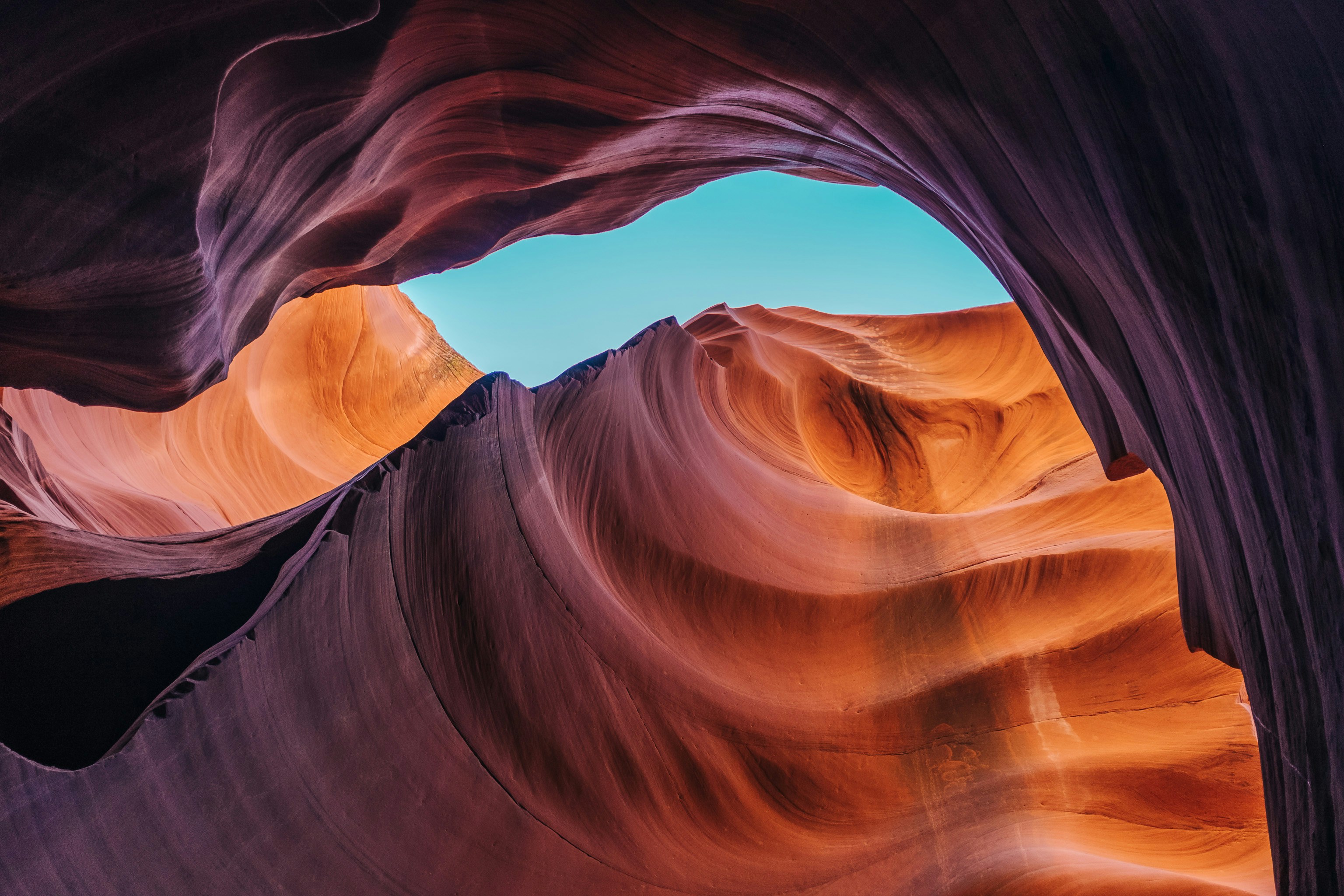 Layered red and purple sandstone walls of a slot canyon curving up to a narrow strip of blue sky