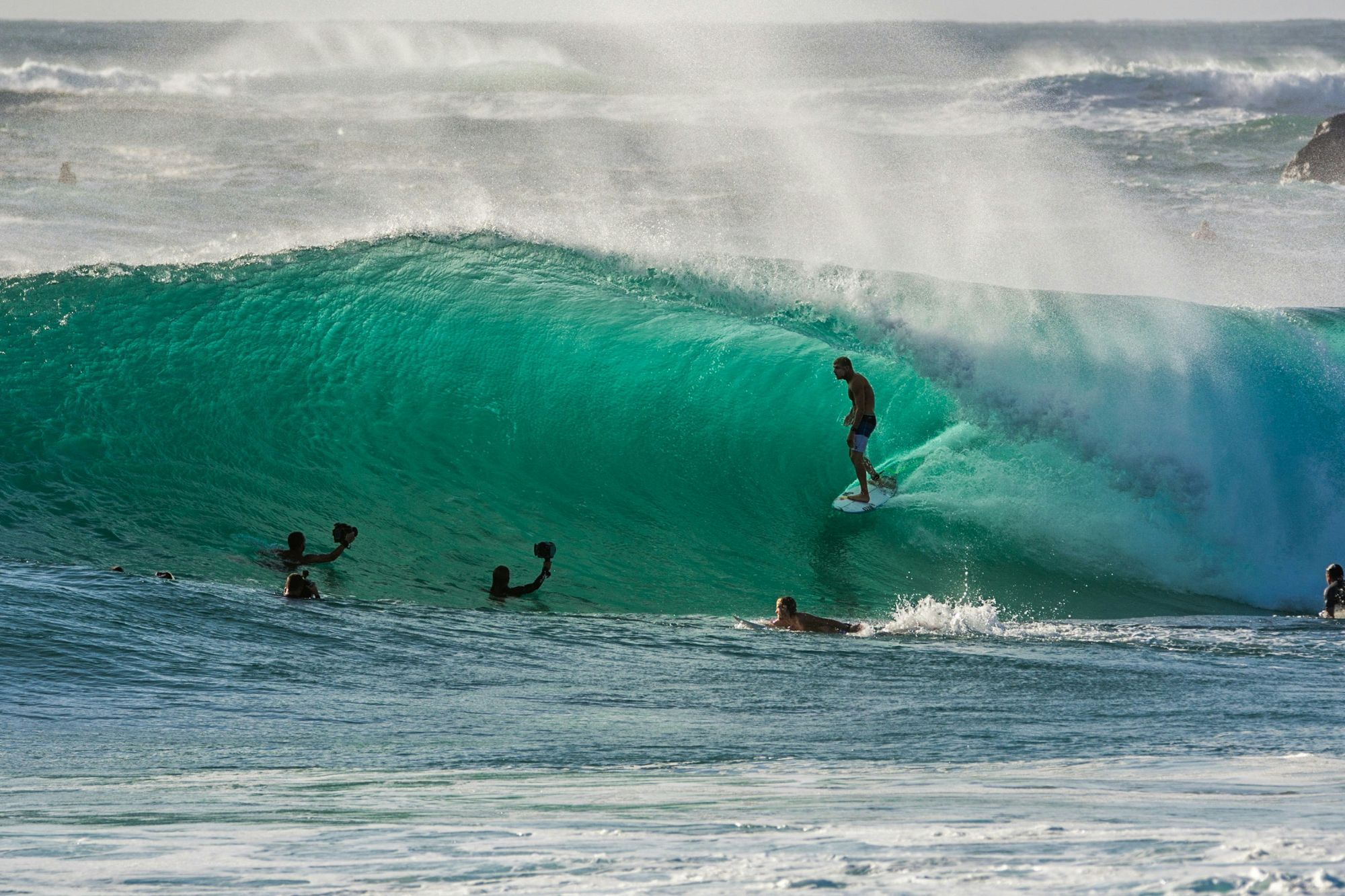 Surfer riding inside the barrel of a turquoise wave as photographers watch from the water